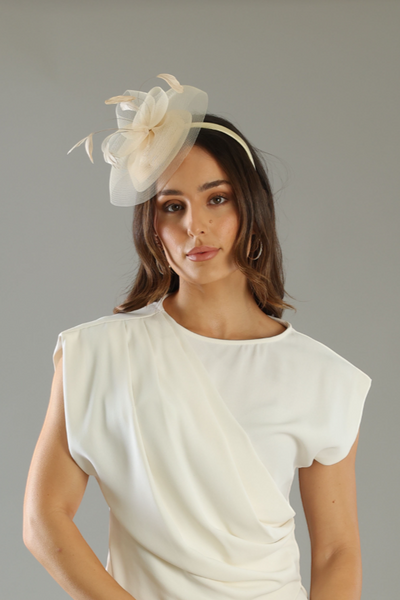 Woman wearing a white outfit with a headband and clutch against a gray background